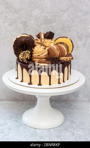 Torta al burro di arachidi decorata con cioccolato fondente scuro, ciambelle, bocconcini di cioccolato, torte, macaroon e caramelle. Sfondo grigio. Foto Stock