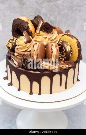 Torta al burro di arachidi decorata con cioccolato fondente scuro, ciambelle, bocconcini di cioccolato, torte, macaroon e caramelle. Sfondo grigio. Foto Stock