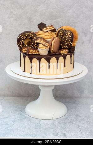 Torta al burro di arachidi decorata con cioccolato fondente scuro, ciambelle, bocconcini di cioccolato, torte, macaroon e caramelle. Sfondo grigio. Foto Stock