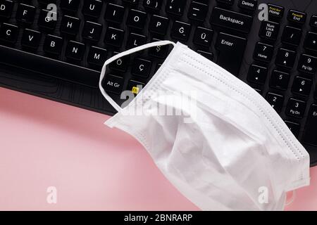 Tastiera per computer e maschera medica protettiva su sfondo rosa. Precauzioni sul posto di lavoro contro il virus corona o covid-19. Foto Stock