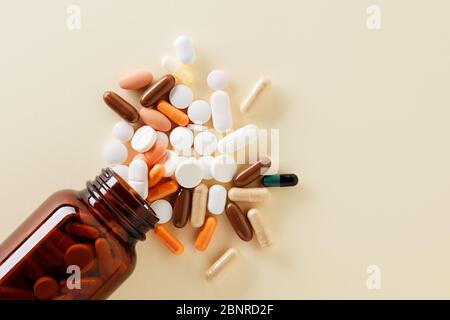 Pillole mediche e compresse fuoriescono da un flacone di farmaco. Vista dall'alto con spazio per la copia su sfondo giallo. Foto Stock