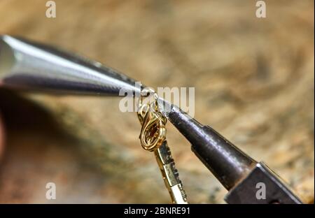 Produzione di gioielli. Il processo di collegamento di una serratura dorata con un bracciale con l'aiuto di due pinze per gioielli. Gioielli fare Foto Stock