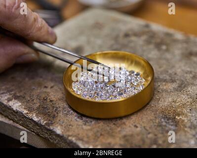 Produzione di gioielli. Diamante trattenuto da pinzette sullo sfondo di diamanti nella piastra per il fissatore Foto Stock