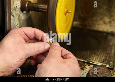 Produzione di gioielli. Gioielleria lucida un anello d'oro su una levigatrice in un laboratorio di gioielli. Foto Stock