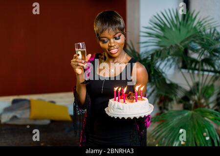 Bella ragazza africana con torta di compleanno e con candele di illuminazione e champagne Foto Stock
