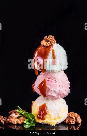 Tre palline colorate di delizioso gelato, su sfondo nero con noci e un rametto di menta. Spazio di copia Foto Stock