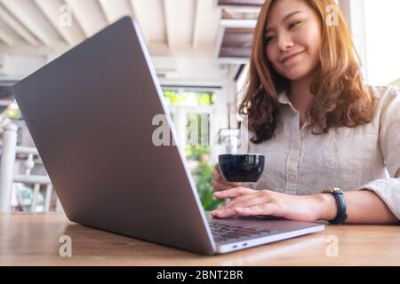 Immagine di una bella donna asiatica che usa e tocca il touchpad del computer portatile mentre beve caffè Foto Stock