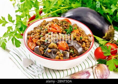 Lenticchie verdi stufate con melanzane, pomodori, aglio e spezie in una ciotola su un tovagliolo, prezzemolo su sfondo di legno Foto Stock