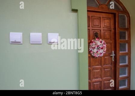 Porta d'ingresso in legno con corona su una casa. Interruttori elettrici a parete Foto Stock