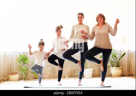 Donne adulte e bambine in linea sul pavimento e stendersi le braccia mentre si fa yoga a casa insieme Foto Stock