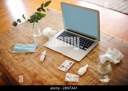 Da sopra vari farmaci e maschera medica posto sul tavolo vicino piante ramoscelli in vaso e laptop con schermo vuoto Foto Stock