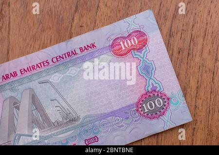 La valuta degli Emirati Arabi Uniti (Emirati Arabi Uniti) - primo piano di una nota rossa cento dirham su uno sfondo marrone tavola. Cambio di denaro. Foto Stock