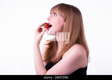 Studio ritratto di una giovane donna sorridente che si muta in una fragola. Foto Stock