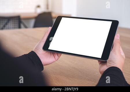 Immagine mockup delle mani che tengono e guardano un tablet pc nero con schermo bianco vuoto mentre si è seduti in ufficio Foto Stock