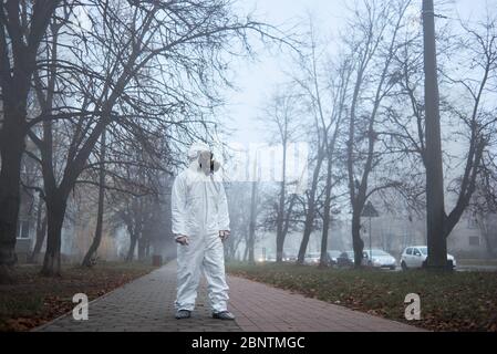 Tutta la lunghezza di ambientalista maschile nel respiratore di sicurezza in piedi sul marciapiede e guardando da parte. Ricercatore che indossa tuta protettiva, maschera a gas. Concetto di ecologia e inquinamento ambientale. Foto Stock