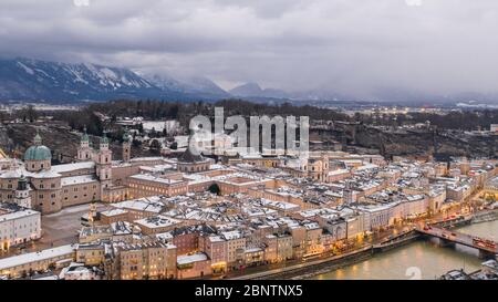 Panoramica aerea del drone di Westside della città vecchia di Salisburgo innevata e della chiesa di Kollegienkirche in Austria in inverno Foto Stock