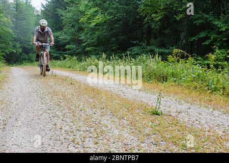 Uomo in bicicletta su Rob Brook Road ad Albany, New Hampshire Stati Uniti. Questa strada sterrata segue parti della vecchia ferrovia Bartlett e Albany che era una terra di tronchi Foto Stock