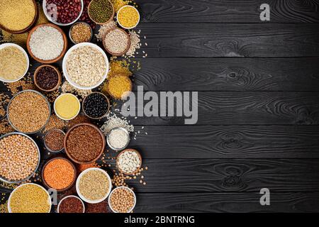 Cereali, cereali, semi, semole, legumi e fagioli in ciotole, vista dall'alto della raccolta di porridge crudo su sfondo di legno nero con spazio per la copia Foto Stock