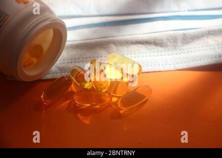 Capsule di olio di pesce Omega 3 che fuoriescono da una bottiglia su uno sfondo arancione e maschera. Concetto di assistenza sanitaria Foto Stock