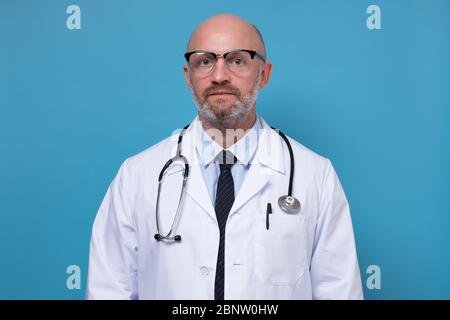 Serio medico medio invecchiato in scrub e cappotto da laboratorio con stetoscopio primo piano Foto Stock