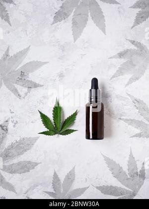 Olio del CBD in bottiglia intorno alle foglie di cannabis su fondo bianco piatto. Spazio libero per il testo Foto Stock