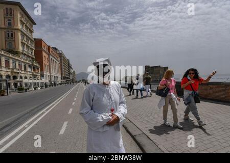 Un artista napoletano vestito da Punch (Pulcinella), maschera della tradizione teatrale napoletana, si esibisce tra le persone sul lungomare di Napoli. L'Italia comincia la fine di un blocco nazionale a causa della diffusione della malattia del coronavirus. Foto Stock