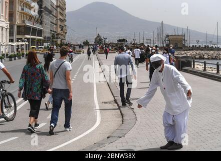 Un artista napoletano vestito da Punch (Pulcinella), maschera della tradizione teatrale napoletana, si esibisce tra le persone sul lungomare di Napoli. L'Italia comincia la fine di un blocco nazionale a causa della diffusione della malattia del coronavirus. Foto Stock