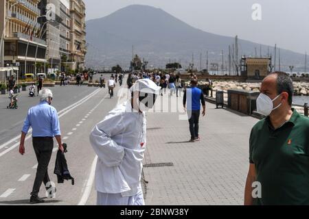 Un artista napoletano vestito da Punch (Pulcinella), maschera della tradizione teatrale napoletana, si esibisce tra le persone sul lungomare di Napoli. L'Italia comincia la fine di un blocco nazionale a causa della diffusione della malattia del coronavirus. Foto Stock