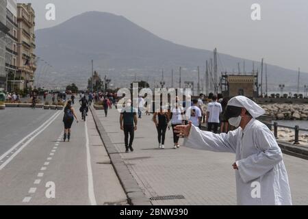 Un artista napoletano vestito da Punch (Pulcinella), maschera della tradizione teatrale napoletana, si esibisce tra le persone sul lungomare di Napoli. L'Italia comincia la fine di un blocco nazionale a causa della diffusione della malattia del coronavirus. Foto Stock