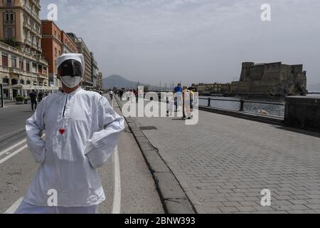 Un artista napoletano vestito da Punch (Pulcinella), maschera della tradizione teatrale napoletana, si esibisce tra le persone sul lungomare di Napoli. L'Italia comincia la fine di un blocco nazionale a causa della diffusione della malattia del coronavirus. Foto Stock