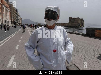 Un artista napoletano vestito da Punch (Pulcinella), maschera della tradizione teatrale napoletana, si esibisce tra le persone sul lungomare di Napoli. L'Italia comincia la fine di un blocco nazionale a causa della diffusione della malattia del coronavirus. Foto Stock