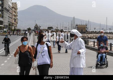 Un artista napoletano vestito da Punch (Pulcinella), maschera della tradizione teatrale napoletana, si esibisce tra le persone sul lungomare di Napoli. L'Italia comincia la fine di un blocco nazionale a causa della diffusione della malattia del coronavirus. Foto Stock