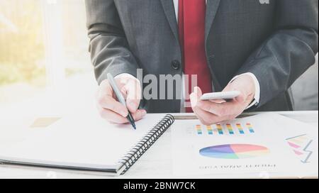 Una sezione centrale di un uomo d'affari alla sua scrivania che analizza e calcola i costi aziendali e la contabilità con i profitti dell'azienda con lo spazio di copia Foto Stock