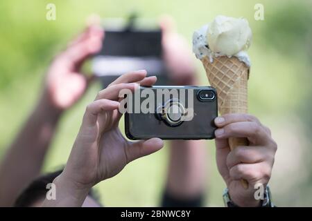 Dresda, Germania. 16 maggio 2020. Un partecipante di un raduno di sostenitori di teorie cospirative sulla crisi di Corona sta tenendo uno smartphone e un gelato nel Grande Giardino. Il Ministro della Sassonia, il Presidente Kretschmer, vuole parlare con i partecipanti al rally. Credit: dpa/dpa-Zentralbild/dpa/Alamy Live News Foto Stock