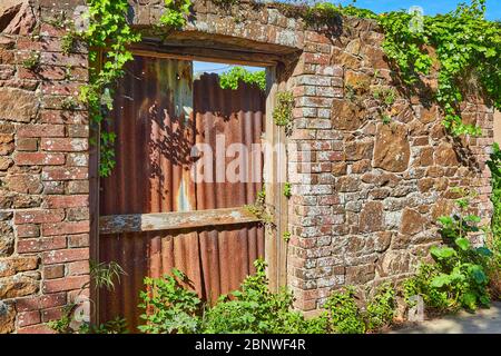 Immagine di un vecchio muro di pietra con una vecchia porta aperta con cornice di mattoni che è stato bloccato con ruggine ferro stheets corigated al sole. Foto Stock