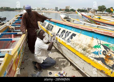 Uomini che riparano una tradizionale barca da pesca Pirogue sulla spiaggia di Soumbediouna, Dakar, Senegal. Foto Stock