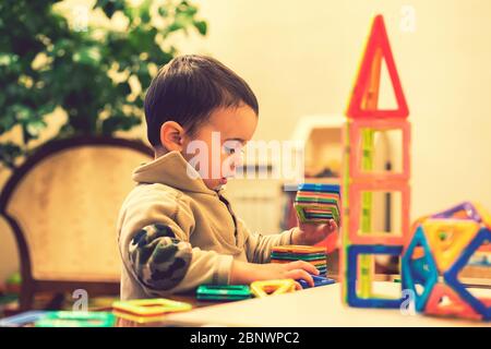 Il ragazzo 2 anni costruire una torre da un costruttore luminoso. Ragazzo sorridente che gioca con il giocattolo costruttore magnetico. Ragazzo che gioca giocattoli intellettuali Foto Stock