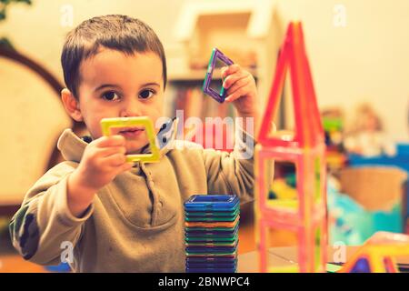 Il ragazzo 2 anni costruire una torre da un costruttore luminoso. Ragazzo sorridente che gioca con il giocattolo costruttore magnetico. Ragazzo che gioca giocattoli intellettuali Foto Stock