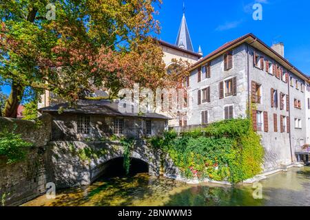 Annecy, Francia: Un edificio su un piccolo ponte di canale nel centro della città vicino Jardin de l'Evêché con Église Notre Dame de Liesse sullo sfondo. Foto Stock