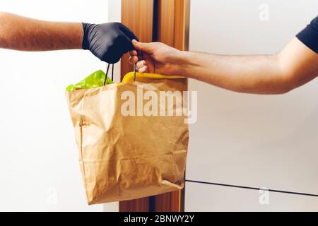 Negozio di alimentari consegna uomo che dà borsa di carta indossare guanti neri come protezione per le precauzioni COVID-19 Coronavirus. Foto Stock