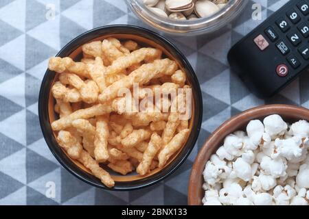 Primo piano di ciotola di popcorn, patatine e telecomando tv su sfondo di legno Foto Stock