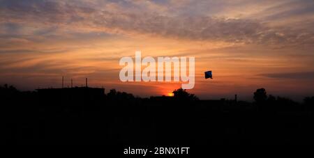 Silhouette di un aquilone che vola in cielo aperto su una città nella stagione estiva, con un bel tramonto sullo sfondo, aquiloni che riflettono i colori, 5K Foto Stock