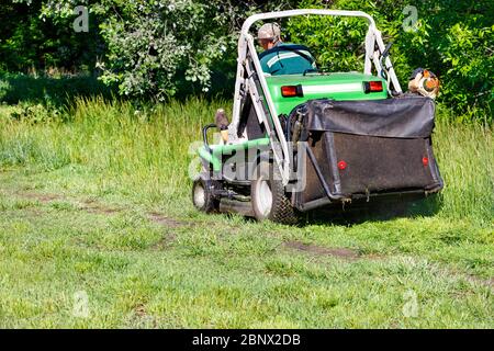 Un addetto ai servizi pubblici taglia erba alta in un giardino in crescita con un rasaerba professionale in una giornata di sole limpida, spazio per le copie. Foto Stock