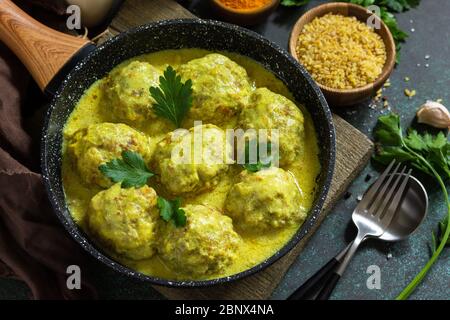 Polpette con bulgaro in panna acida e salsa curcuma in una padella su un piano di pietra scuro. Foto Stock