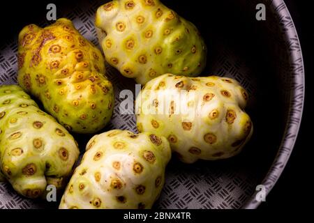 Noni o frutta di formaggio raggruppati con varie tonalità di colore contrastate con una superficie metallica scura di una padella. Cibo da studio ancora basso Foto Stock