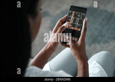 Donna nera giocando Sudoku sul telefono per l'addestramento del cervello Foto Stock