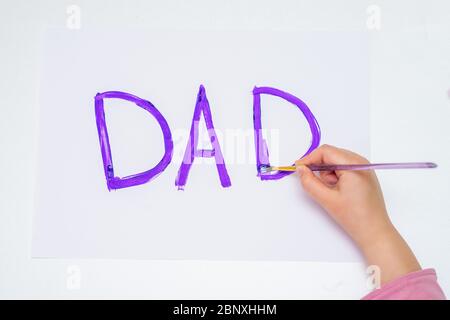 Vista dall'alto della mano del bambino che disegnano la parola viola biglietto d'auguri papà su carta bianca. Concetto di Giornata del Padre felice. Foto Stock