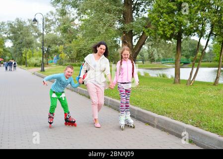 Donna aiuta i bambini a pattinare nel Parco Foto Stock