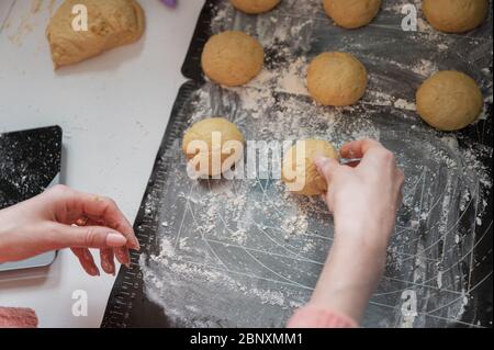 Mani femminili mettendo palle di pasta rotonde su un tappetino per sollevarsi. Foto Stock