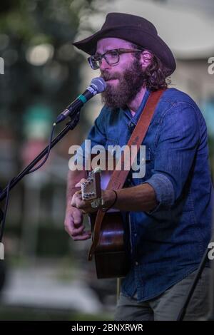 Cantante folk bearded che si esibisce in un concerto di outdoor. Cantare e suonare la chitarra acustica. Foto Stock